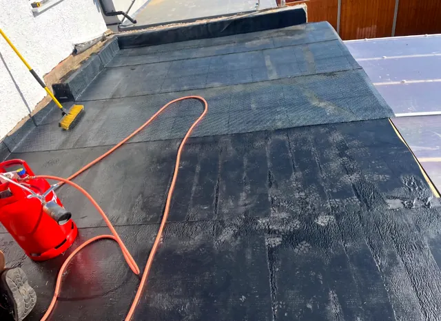 A torch-on felt flat roof being laid, with the gas torch and bottle beside it